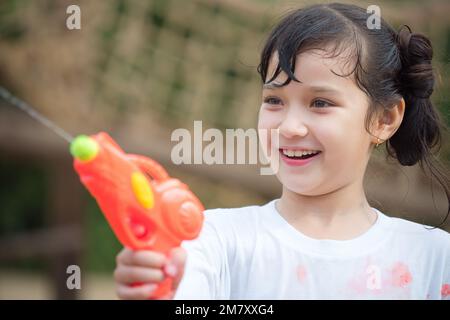 Happy Child girl s'amuse à jouer au tir au pistolet à eau sur une aire de jeux en plein air le jour d'été chaud à l'extérieur. Banque D'Images