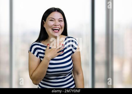 Portrait d'une jeune femme asiatique heureuse riant dur à l'intérieur. Arrière-plan de fenêtres flou. Banque D'Images