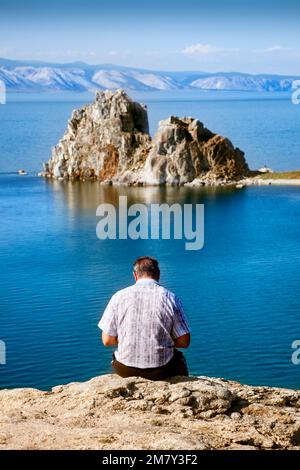 Olkhon, Russie-27 juillet 2010. Un homme assis sur une falaise lisant un livre en face ok Cape Burkhan Banque D'Images