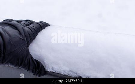 Main dans le gant en cuir noir gros plan sur la main courante enneigée du pont sur fond blanc enneigé Banque D'Images