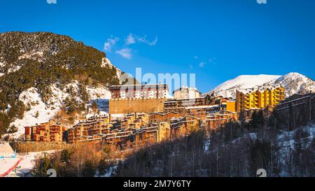 Lumière du coucher de soleil illuminant la ville de Soldeu entourée d'une forêt de pins et d'une chaîne de montagnes enneigée. Vacances d'hiver au ski en Andorre, Pyrénées Banque D'Images