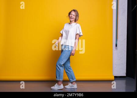 Vue sur toute la longueur d'une femme magnifique portant un Jean debout à l'intérieur en studio. Jolie femme riant. Portrait de mode studio. Pleine longueur Banque D'Images