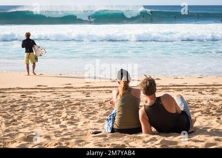 Un jeune surfeur et un couple regardent le surf à grandes vagues Banque D'Images