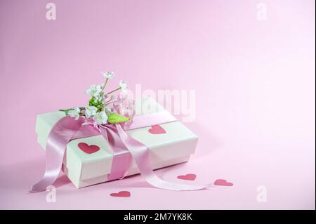 Boîte cadeau avec bouquet de fleurs, ruban et formes de coeur en papier sur fond rose clair, carte de voeux pour la Saint-Valentin, la fête des mères ou le mariage, Banque D'Images