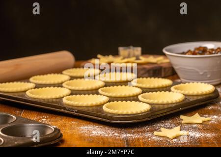 Vue latérale d'un plateau métallique de pâtisseries non cuites avec bords cannelés prêts à être faits dans des tartes hachées. Cuisson de Noël Banque D'Images