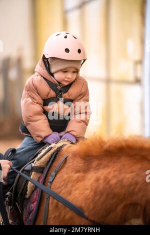 Leçon de équitation pour les petits enfants. Une jeune fille de trois ans fait du poney et fait des exercices Banque D'Images