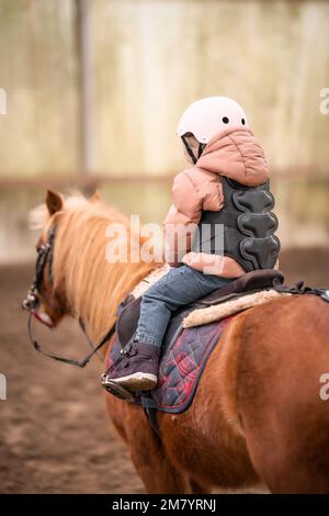 Leçon de équitation pour les petits enfants. Une jeune fille de trois ans fait du poney et fait des exercices Banque D'Images