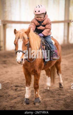 Leçon de équitation pour les petits enfants. Une jeune fille de trois ans fait du poney et fait des exercices Banque D'Images