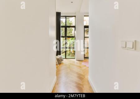 un couloir vide avec parquet et murs blancs, menant à la porte d'entrée qui mène au jardin Banque D'Images