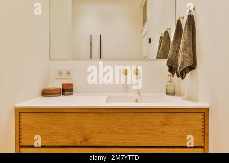 une salle de bains avec un miroir au-dessus du lavabo et une serviette accrochée au mur à côté de la coiffeuse dans la chambre Banque D'Images