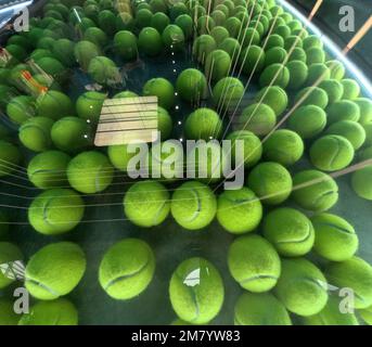 plusieurs balles de tennis derrière un verre avec des reflets lumineux sur fond vert et gris Banque D'Images