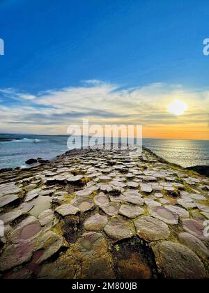 Vue sur un coucher de soleil depuis la chaussée du géant avec des briques structurées sur la mer. Banque D'Images