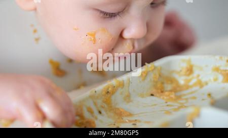 Bébé fille saisit les restes de nourriture et mange avec enthousiasme Banque D'Images