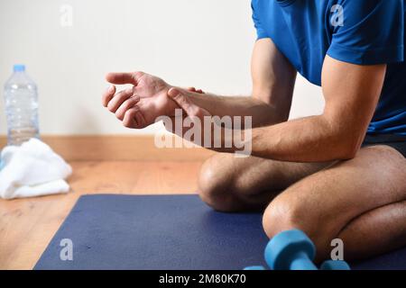 Détail de l'homme faisant du sport avec douleur de poignet se tenant avec sa main assise sur un tapis. Vue latérale Banque D'Images