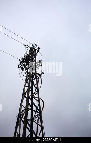 Pylône d'électricité avec des câbles de tête passant dessus et un ciel nuageux comme arrière-plan Banque D'Images