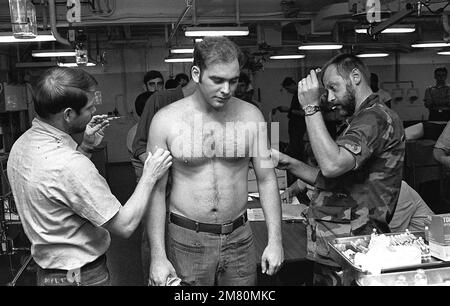 Les hommes de l'hôpital classe 2nd (HM2) Dennis Boyles (à gauche) et William Healy donnent des coups de feu à un homme d'équipage à bord du navire d'assaut amphibie USS TARAWA (LHA-1). Pays : inconnu Banque D'Images