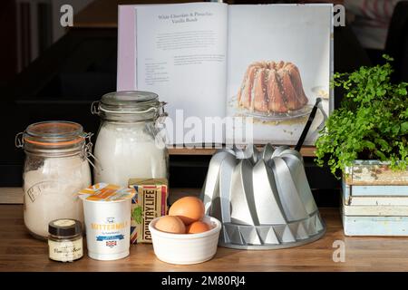 Ingrédients pour la fabrication de gâteaux regroupés sur un plan de travail de cuisine avec un moule à pain Nordic Ware. Les ingrédients sont pour faire un gâteau montré dans un livre ouvert Banque D'Images