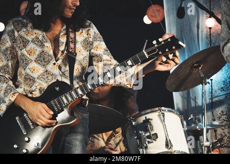 Un jeune homme méconnaissable aux cheveux longs jouant de la guitare électrique comme membre d'un groupe de rock and roll sur scène Banque D'Images