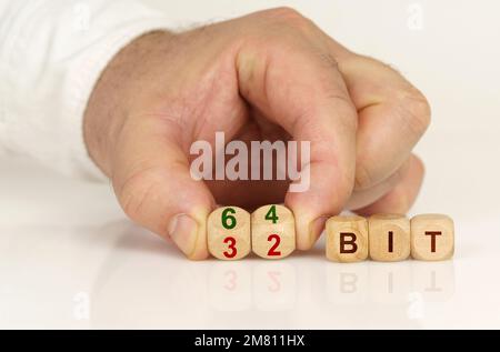 Sur une surface blanche réfléchissante dans les mains d'un homme sont des cubes avec l'inscription - 64 ou 32 bits. Concept de technologie Banque D'Images