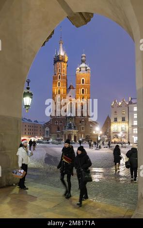 L'église Saint-Marys de Cracovie éclairée la nuit ; vue à travers une arche de la salle des tissus en hiver, place du marché principal de Cracovie, vieille ville de Cracovie, Pologne de Cracovie Banque D'Images