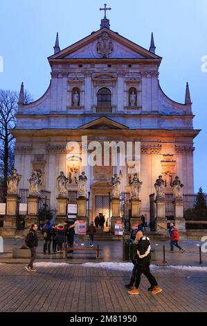 Scène de la rue de Cracovie - personnes marchant devant l'église des Saints Pierre et Paul lors d'une soirée d'hiver, vieille ville de Cracovie, Cracovie Pologne Europe Banque D'Images