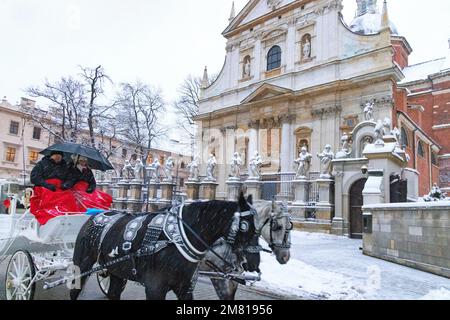 Le tourisme de Cracovie - un cheval et une calèche passent devant l'église des Saints Pierre et Paul dans la neige d'hiver, Cracovie Pologne Europe Banque D'Images