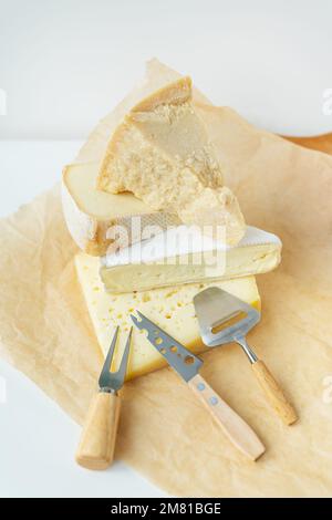 Différents types de fromage se trouvent l'un sur l'autre avec des couteaux à fromage sur parchemin. Une délicieuse délicatesse. Photo verticale Banque D'Images