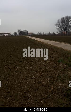 Route étroite entre les champs labourés par une journée nuageux dans la campagne italienne Banque D'Images