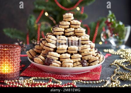 Un tas de biscuits de Noël faits maison remplis de marmelade et trempés dans du chocolat, avec une décoration rouge et dorée Banque D'Images