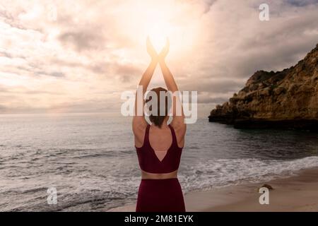 Vue arrière d'une femme méditant en plongeant le soleil dans ses mains au bord de la mer. Banque D'Images