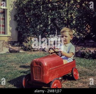 Un garçon de deux ans conduit un tracteur jouet dans un jardin en 1959. Cette photo a été prise à partir de la diapositive d'origine. Banque D'Images