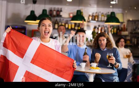 Crier les jeunes fans de sport pour adultes qui se sont pris pour l'équipe préférée et qui ont le drapeau du Danemark tout en regardant le match ensemble au pub Banque D'Images