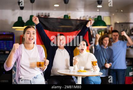 Compagnie de hurler de jeunes adultes fans de sport en signe de drapeau de l'Allemagne et en soutenant l'équipe nationale avec de la bière dans le pub Banque D'Images