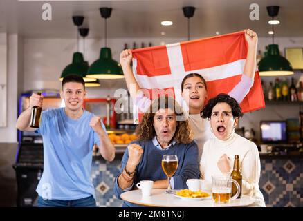 Crier les jeunes fans de sport pour adultes qui se sont pris pour l'équipe préférée et qui ont le drapeau du Danemark tout en regardant le match ensemble au pub Banque D'Images