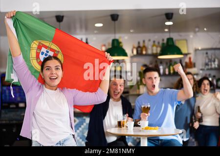 Compagnie de jeunes fans de sports adultes hurlant le drapeau du Portugal et soutenant l'équipe nationale avec de la bière dans le pub Banque D'Images