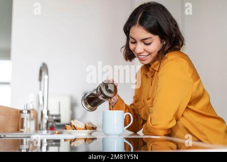 Gros plan de la jeune femme arabe souriante qui verse le café du matin à la tasse Banque D'Images