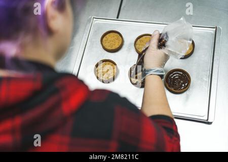 Point de vue de haut angle de chef de boulangerie professionnel décorant des tartes de chocolat avec l'utilisation de sac de pâtisserie. Photo de haute qualité Banque D'Images