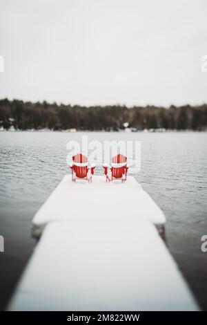 Chaises red adirondack muskoka au bout du quai enneigé en hiver. Banque D'Images