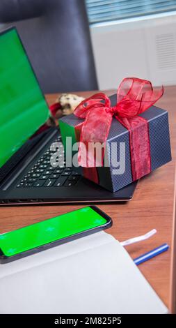 Ordinateur portable maquette écran vierge grrn avec boîte cadeau et téléphone avec écran vert sur le bureau. Cadeau de Saint-Valentin, amour, coeur, achats en ligne Banque D'Images