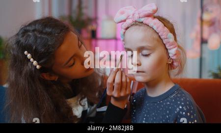 L'enfant adolescent aide ou enseigne à faire le maquillage du visage de sa petite sœur, fille d'enfant. Femmes frères et sœurs enfants meilleurs amis mettant l'application de maquillage cosmétique à la salle de jeux à la maison. Amitié, relation de famille Banque D'Images