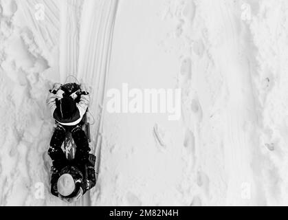 Au-dessus de l'avion fait la photo de deux enfants dans un traîneau descendant une colline enneigée. Banque D'Images