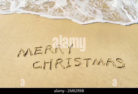 Joyeux Noël à la main dans le sable sur la plage Banque D'Images