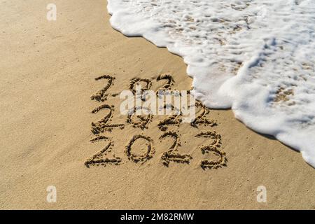 2023 et 2022 inscription écrite dans le sable humide de la plage avec la vague d'eau de mer. Banque D'Images