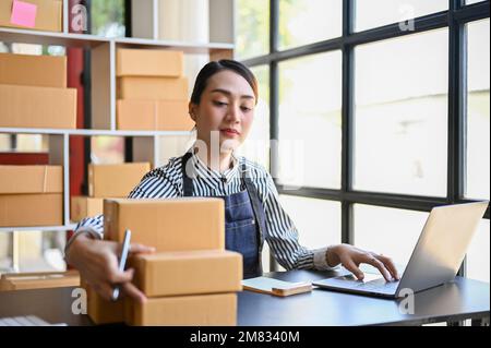 Femme asiatique millénaire spécialisée propriétaire de boutique en ligne travaillant dans son bureau à domicile, utilisant un ordinateur portable, gérant ses commandes d'expédition. Banque D'Images