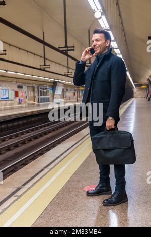Photo verticale d'un homme d'affaires d'âge moyen du Caucase parlant au téléphone en attendant le train Banque D'Images