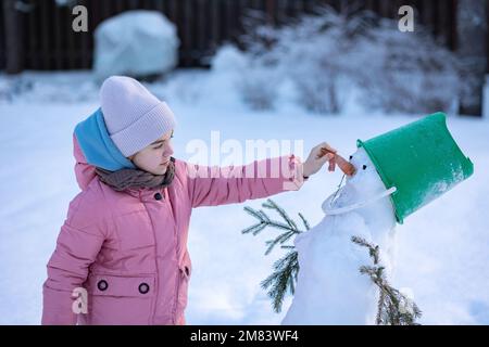 Une petite fille fait bonhomme de neige l'hiver par temps froid. L'enfant fait le nez de la carotte. . Photo de haute qualité Banque D'Images