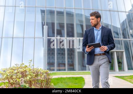 Un beau jeune homme d'affaires se promenant dans un parc d'affaires à l'extérieur du bureau avec une tablette Banque D'Images
