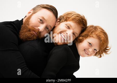 portrait de famille d'un homme barbu à tête rouge avec son fils et son petit-fils souriant à l'appareil photo isolé sur image grise Banque D'Images