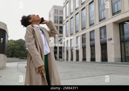 une jeune femme afro-américaine qui parle sur un téléphone portable dehors avec sa tête a été jetée en arrière et a ri Banque D'Images