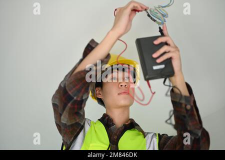 Électricien asiatique à l'aide d'un multimètre mesurant la tension et le courant d'une ligne électrique de puissance Banque D'Images